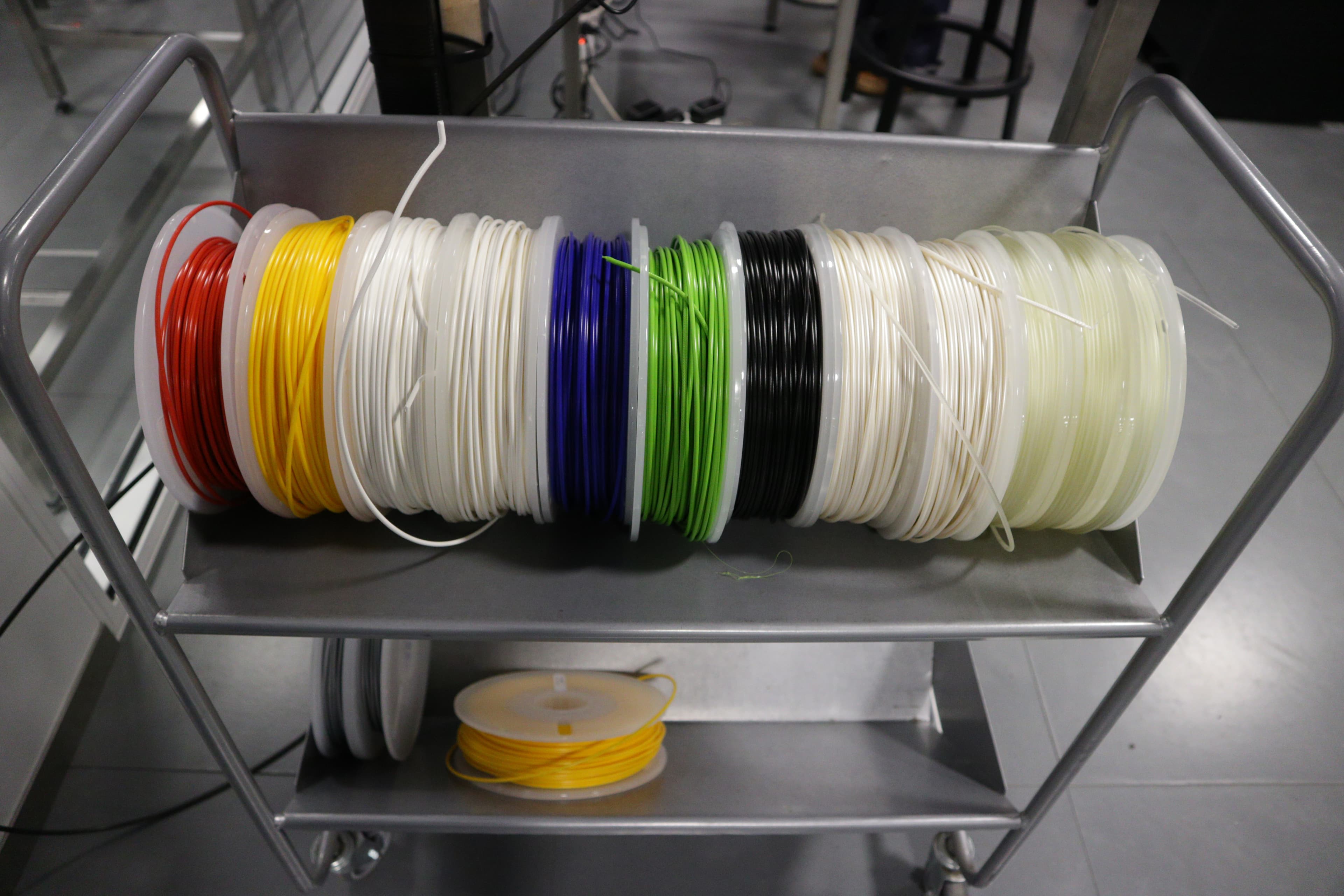 Stacked spools of colored 3D printing filament on a shelf