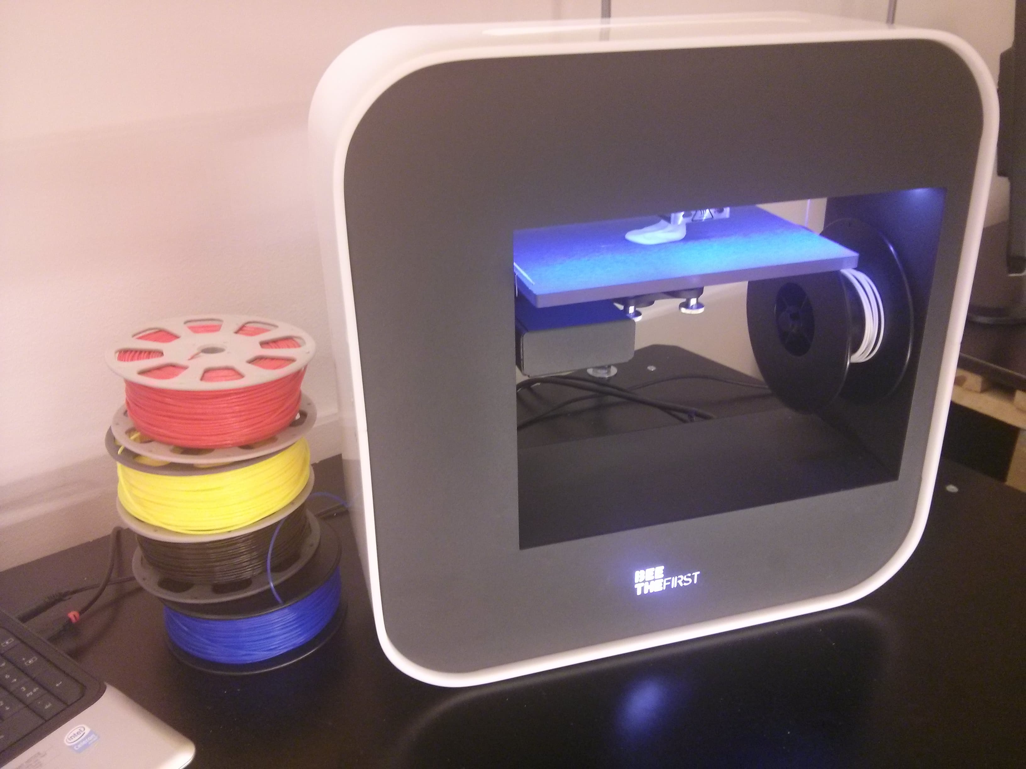 A 3D printer next to colored filament spools on a workbench